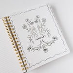 2026 Meadow Weekly Planner open to January page with floral illustrations and gold spiral binding.