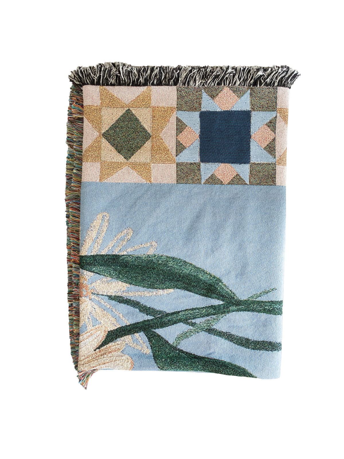 Folded light blue woven fabric blanket with fringed edges, featuring green leaves and geometric star patterns.