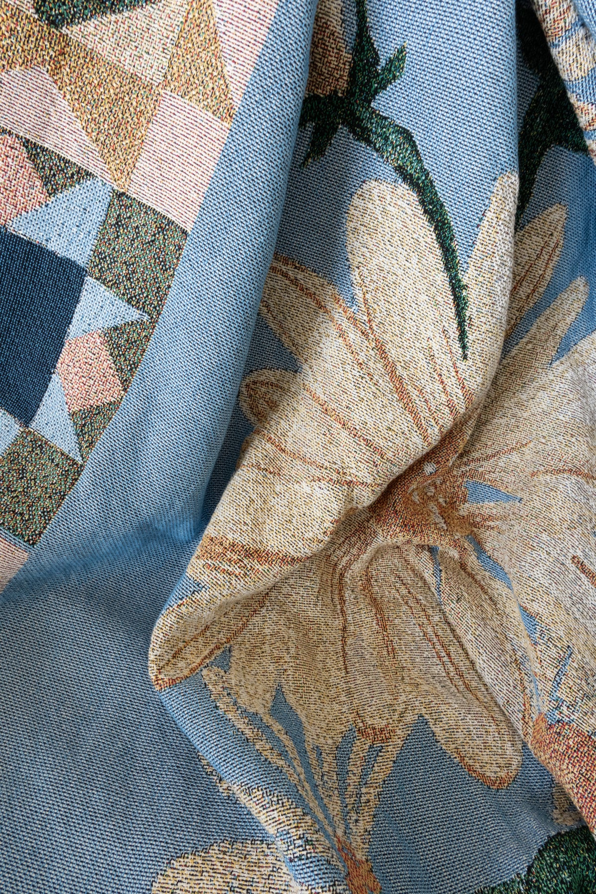 Close-up of a blue woven fabric blanket featuring a large cream flower and a geometric border of multicolored triangles.