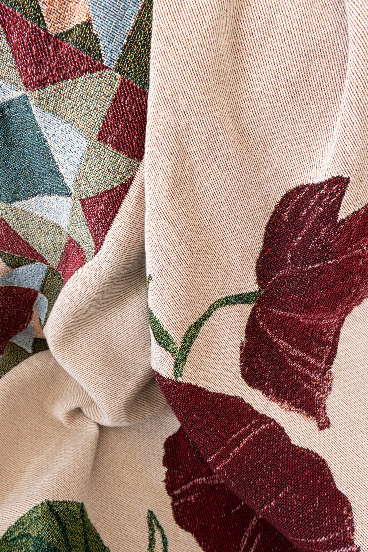 Draped cream woven fabric featuring a red floral pattern and a geometric design in red, blue, and green.