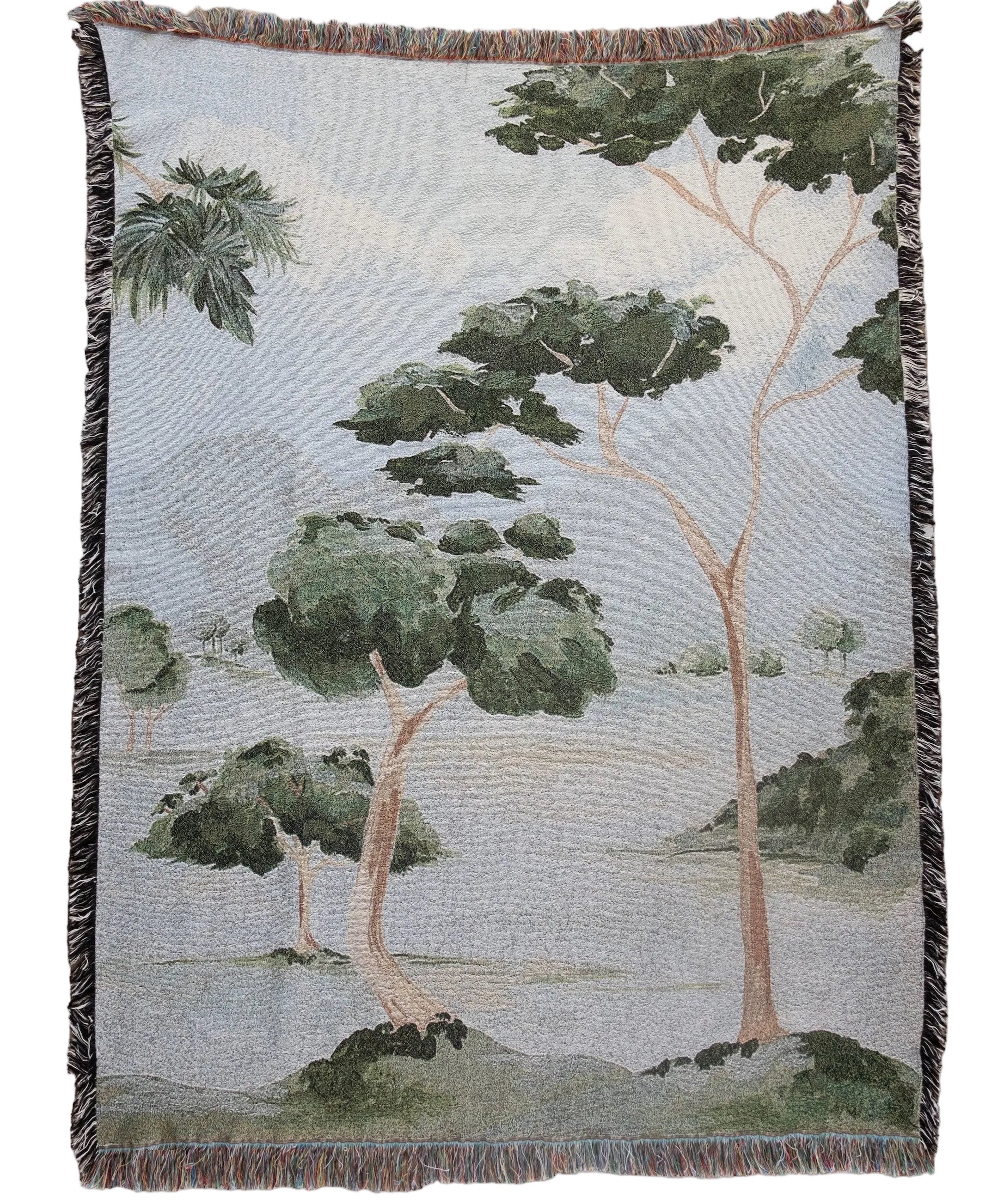 Woven blanket with a nature-themed design of trees and landscape on a plain background