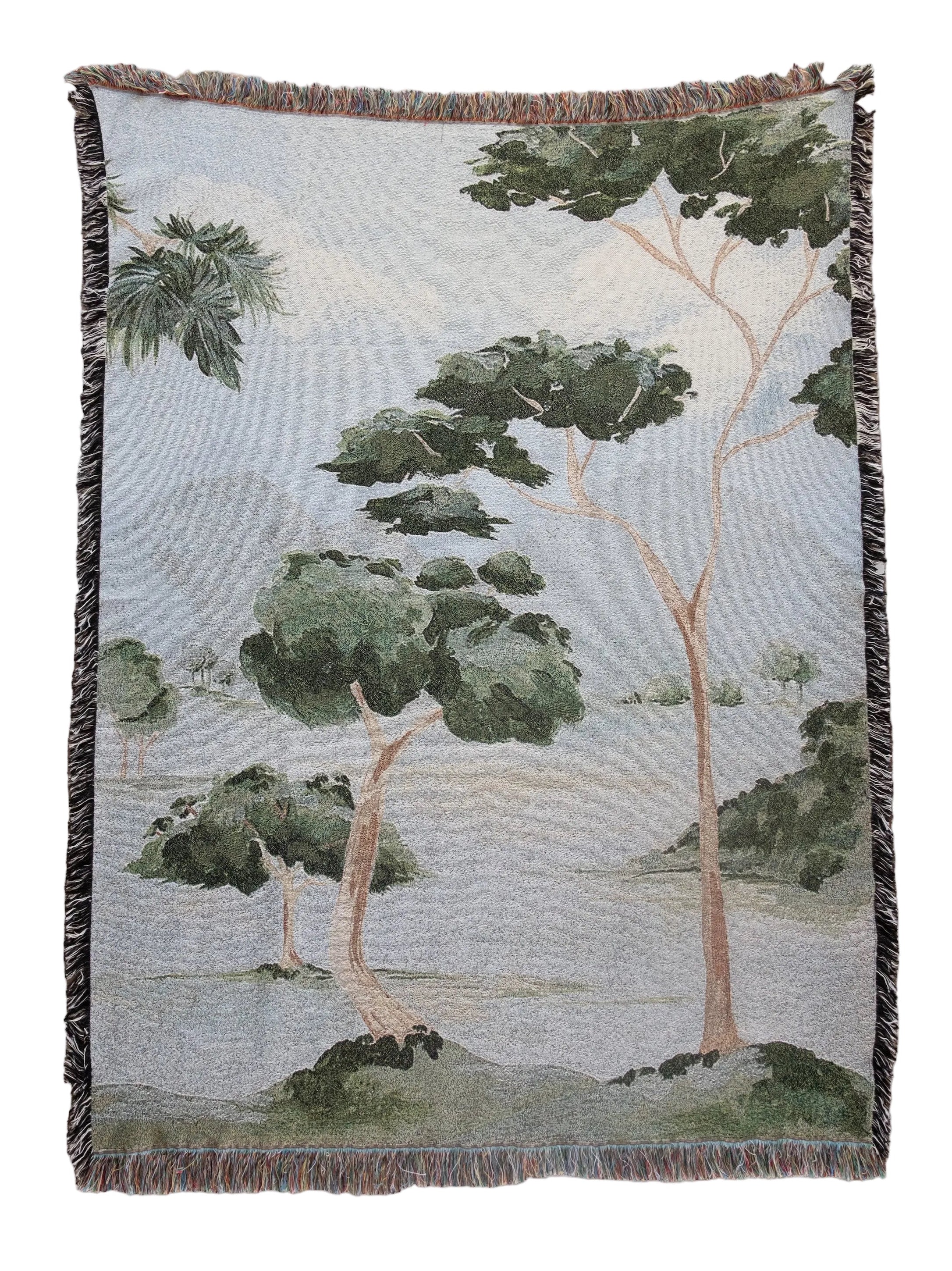 Woven blanket with a nature-themed design of trees and landscape on a plain background