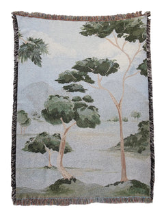 Woven blanket with a nature-themed design of trees and landscape on a plain background