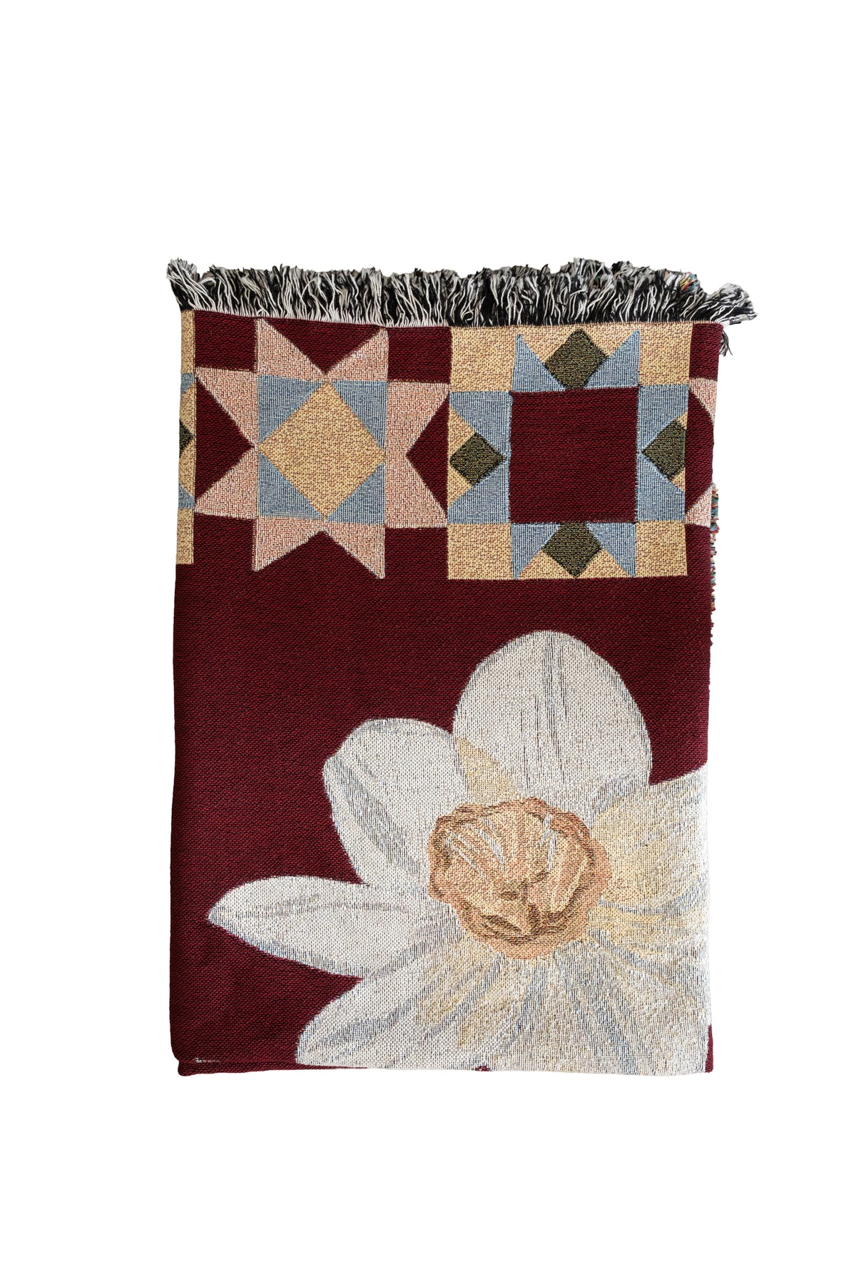 Folded burgundy woven blanket with a large white flower and geometric star patterns in blue, gold, and tan with fringe.