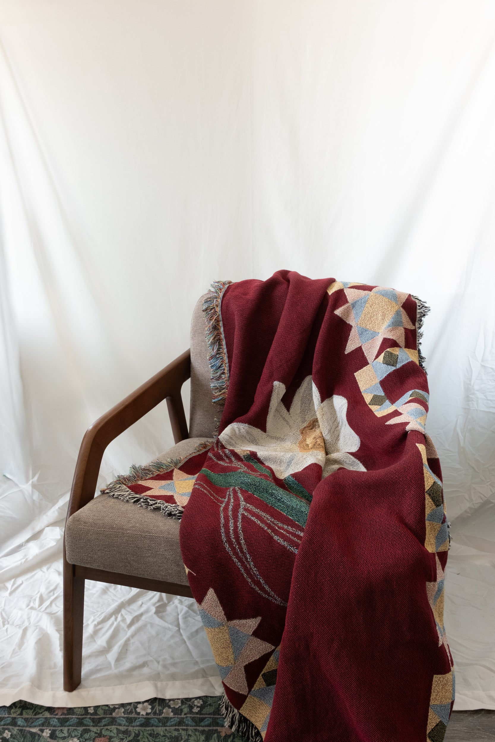 Burgundy woven fabric blanket with a white flower and geometric patterns draped over a wooden chair.