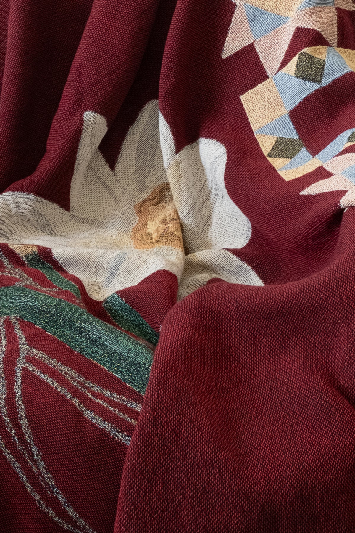 Draped burgundy woven fabric featuring a large white flower, green leaves, and a geometric pattern in tan and blue.