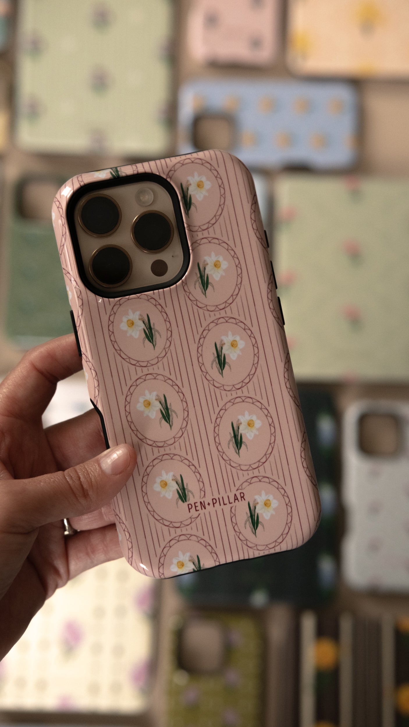 Pink plastic iPhone case with white narcissus flowers in circles and vertical stripes, printed with PEN+PILLAR.