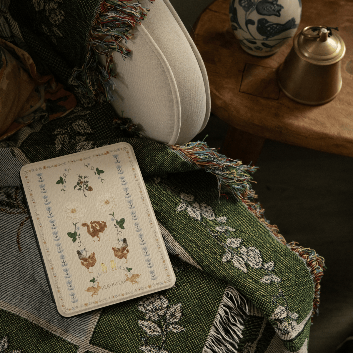 Farmland Kindle case on a green quilt beside a cream ceramic vase