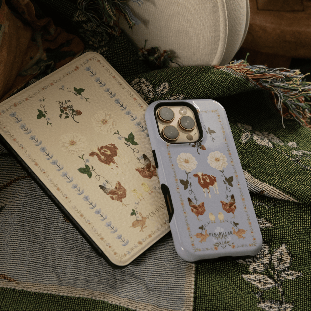 Farmland iPhone case resting on a cream Kindle case printed with hens and florals, on a green quilt
