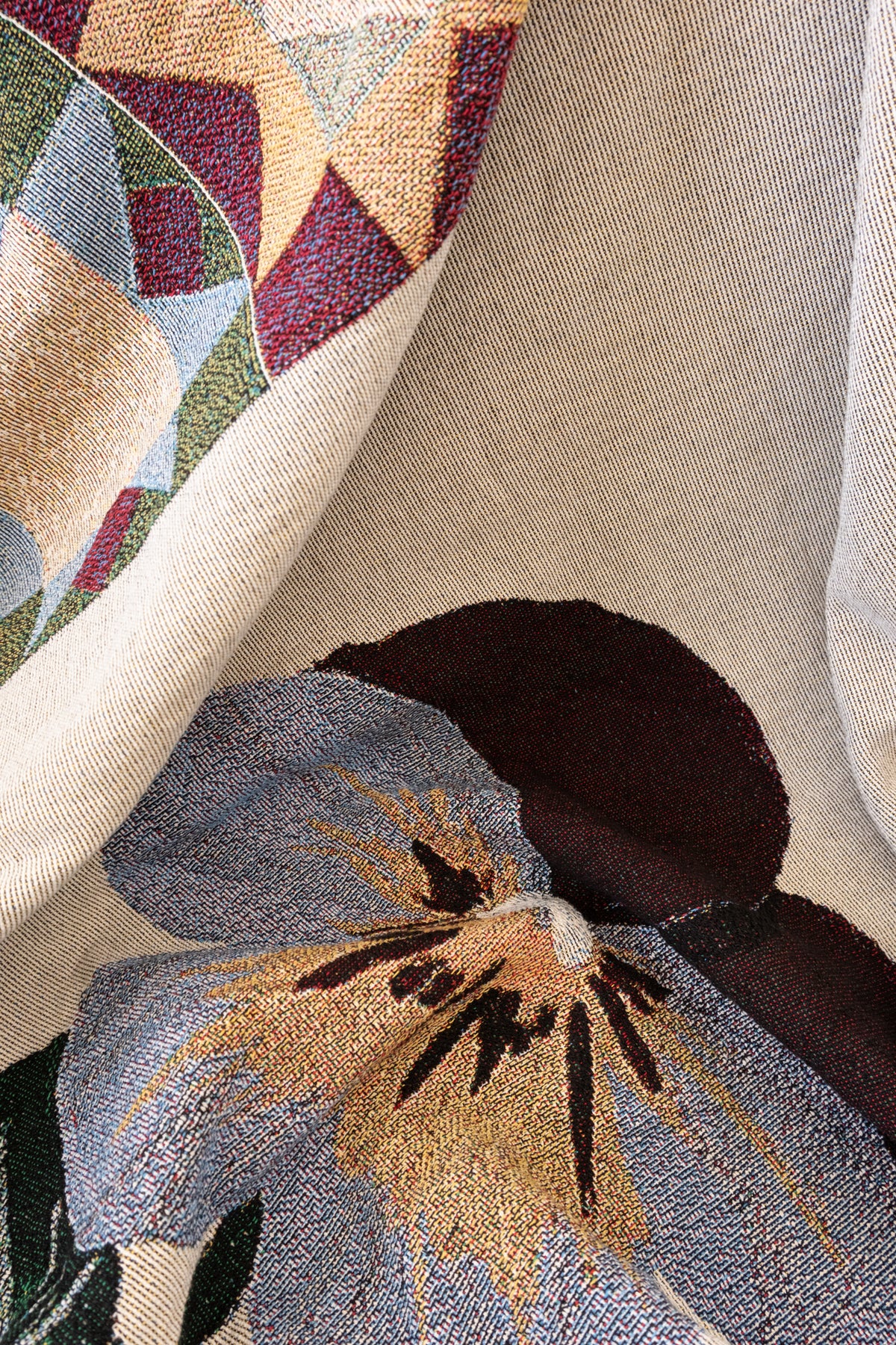 Close-up of a woven fabric blanket featuring a large purple and yellow pansy flower and geometric patterns.