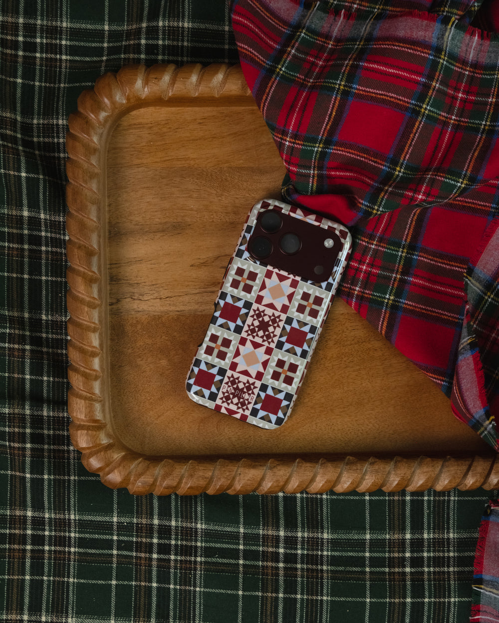 Holiday Sampler phone case on a carved wooden tray over red and green plaid
