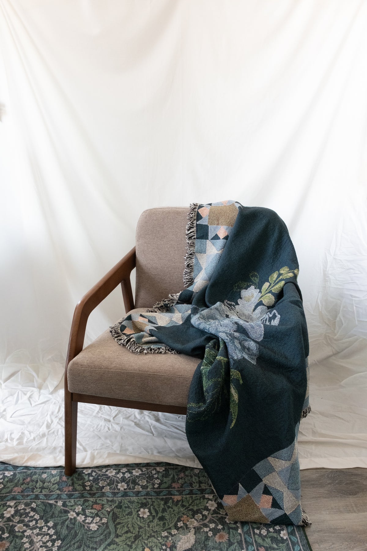 Dark green woven blanket with floral and geometric patterns draped over a brown fabric and wood chair.