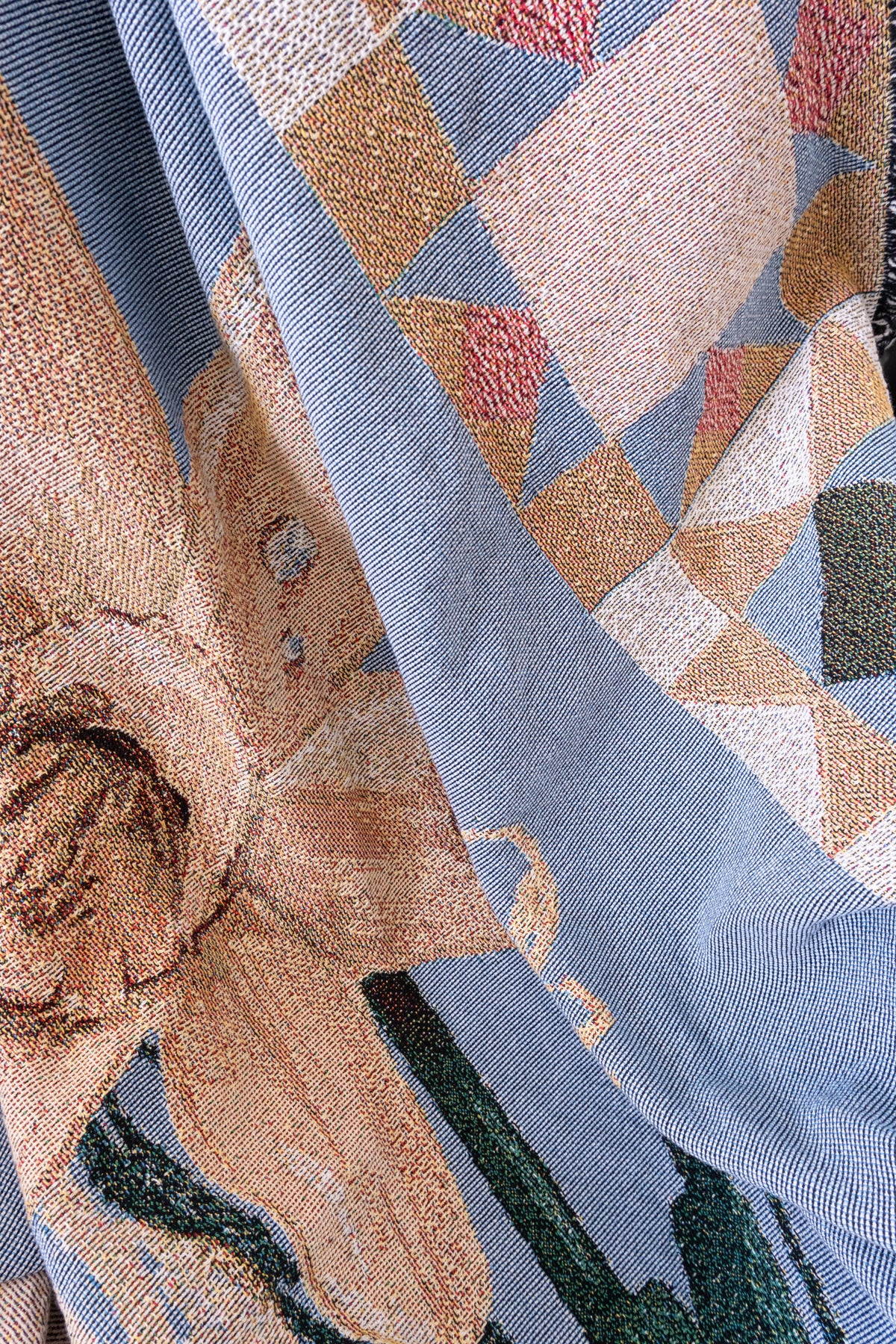 Blue and tan woven fabric blanket featuring a large daffodil flower and geometric triangle patterns.