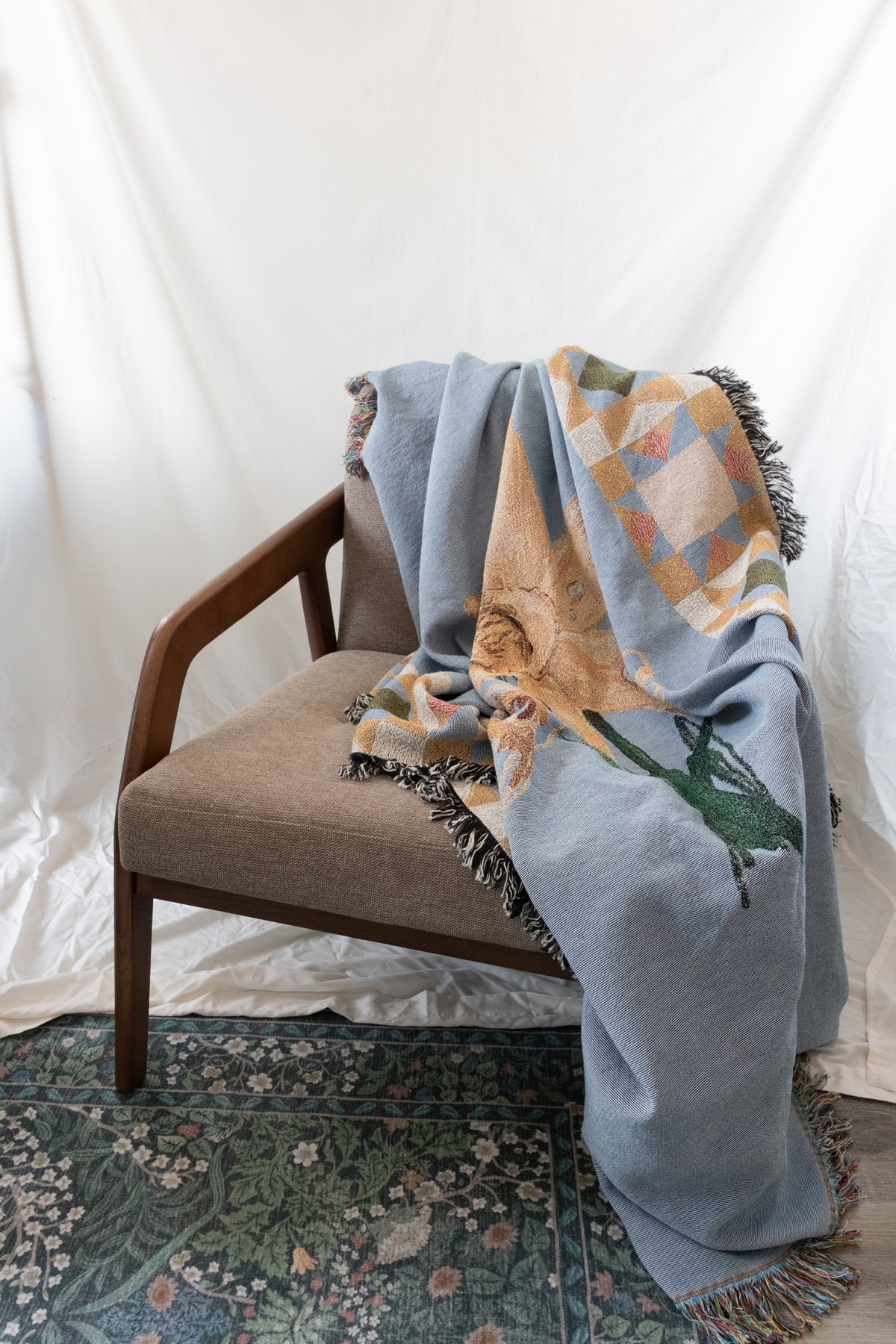 Blue woven fabric blanket with fringe and floral pattern draped over a wood and fabric armchair.