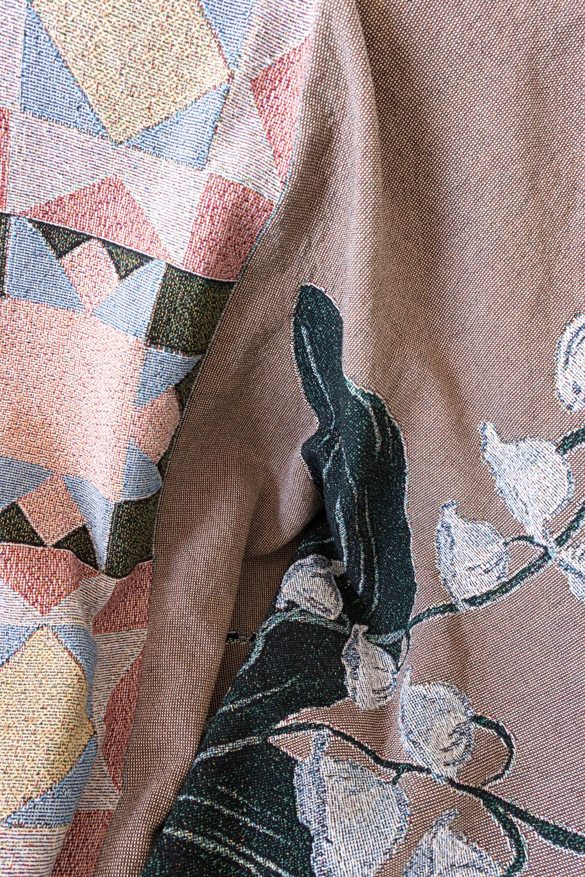 Close-up of a brown woven fabric blanket featuring a white floral pattern and a colorful geometric triangle design.