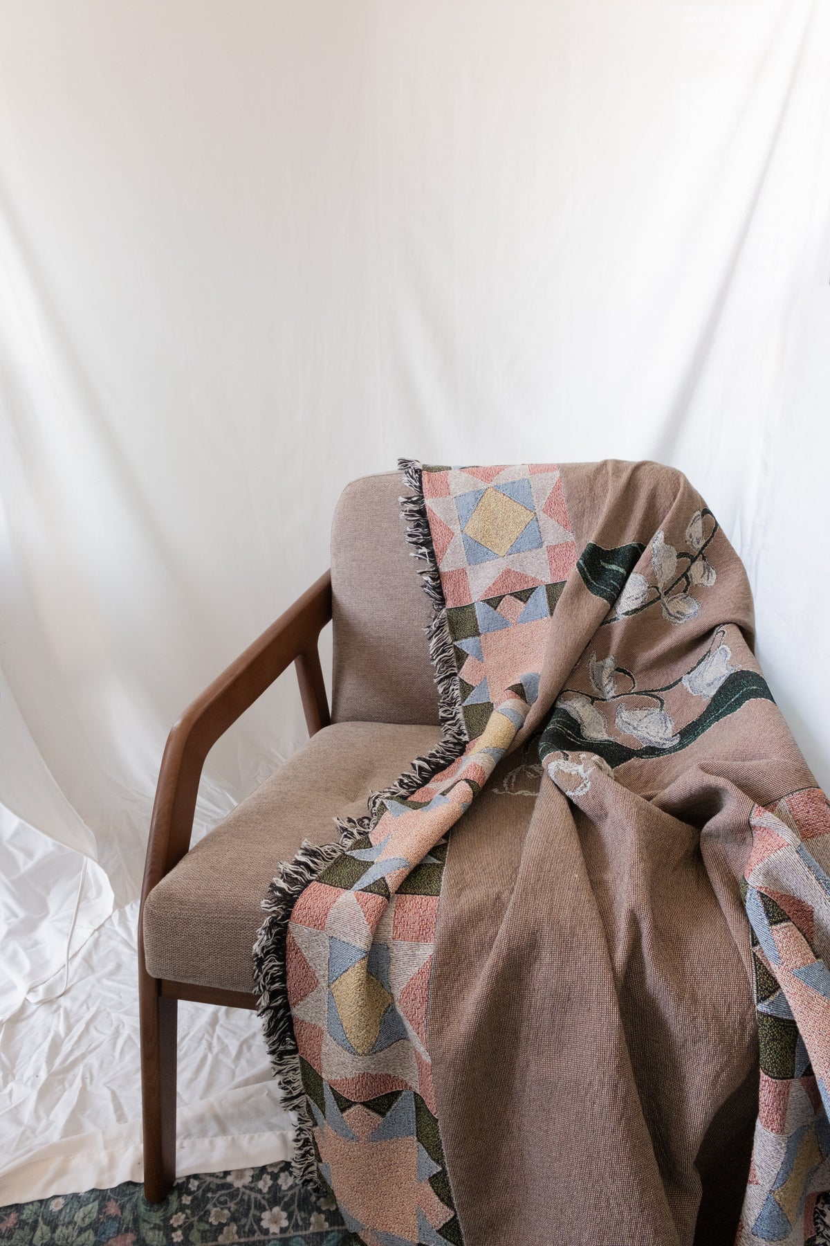 Brown woven May Birth Month Woven Blanket with floral and geometric patterns draped over a fabric and wood chair.