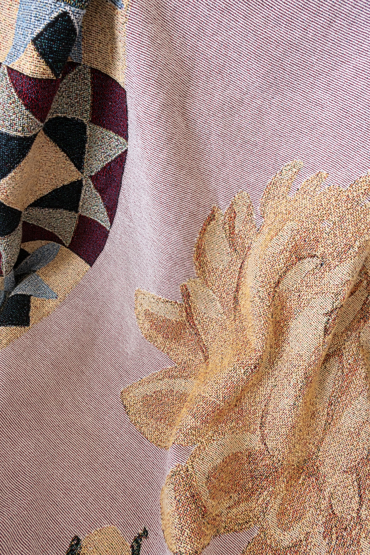 Close-up of a woven fabric blanket featuring a yellow floral pattern and a geometric circular design in red and black.