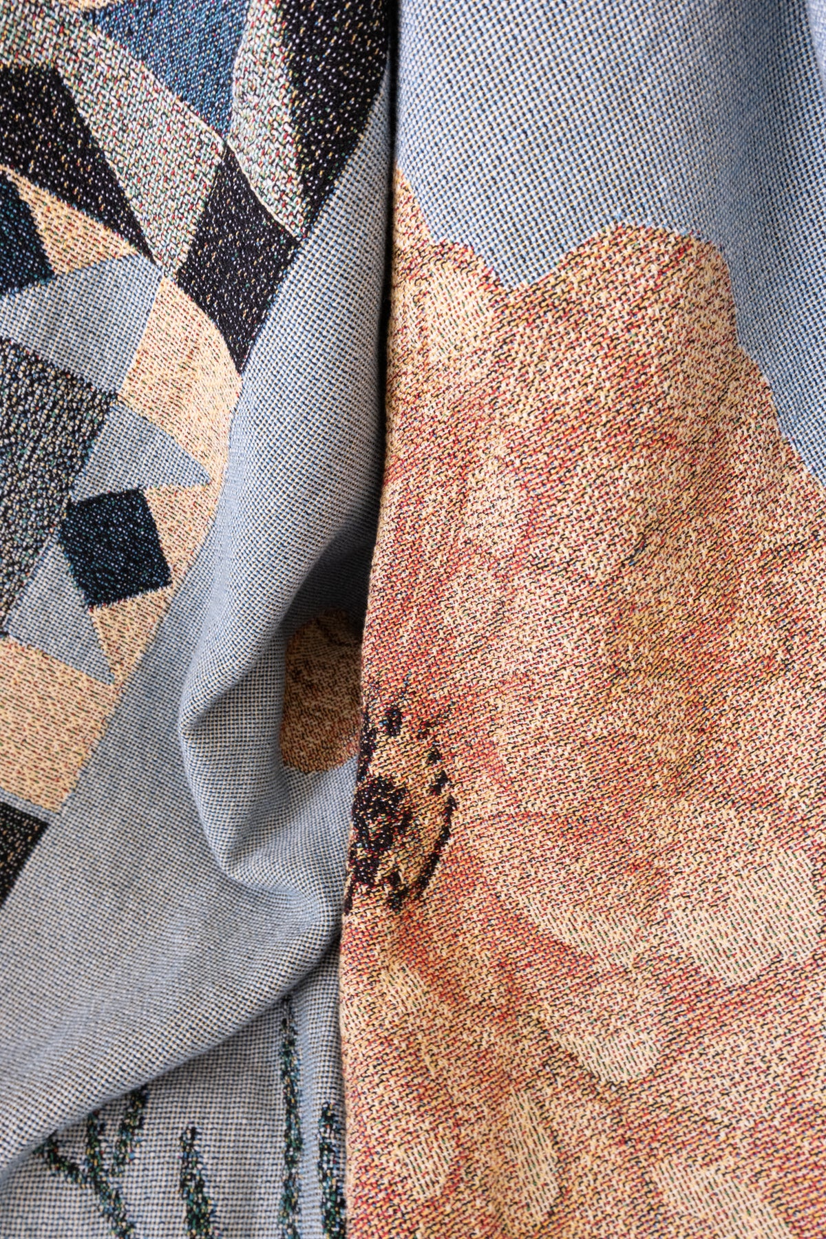 Draped blue woven fabric featuring a peach floral pattern and a geometric diamond design in tan and navy.