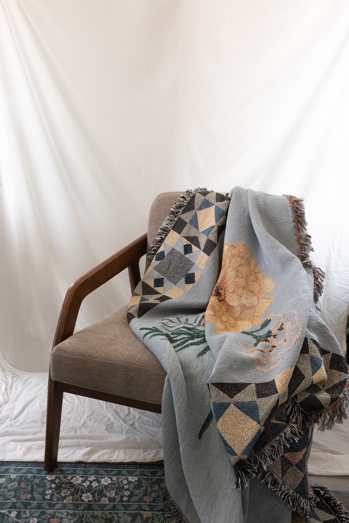 Blue woven fabric blanket with fringe, floral marigold design, and geometric borders draped over a brown wood and fabric c...