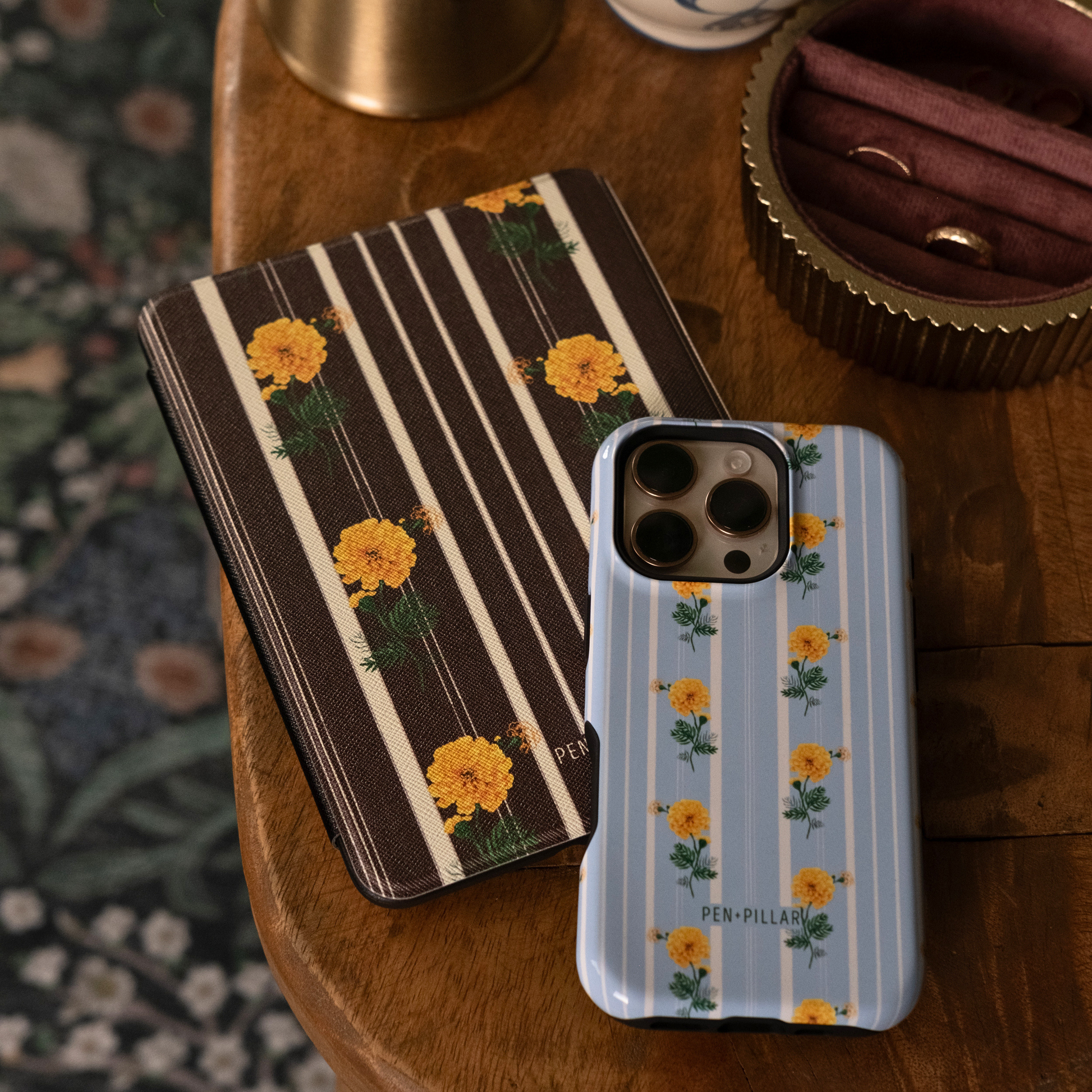 Brown striped Kindle case and light blue phone case, both with yellow flower patterns and PEN PILLAR branding.