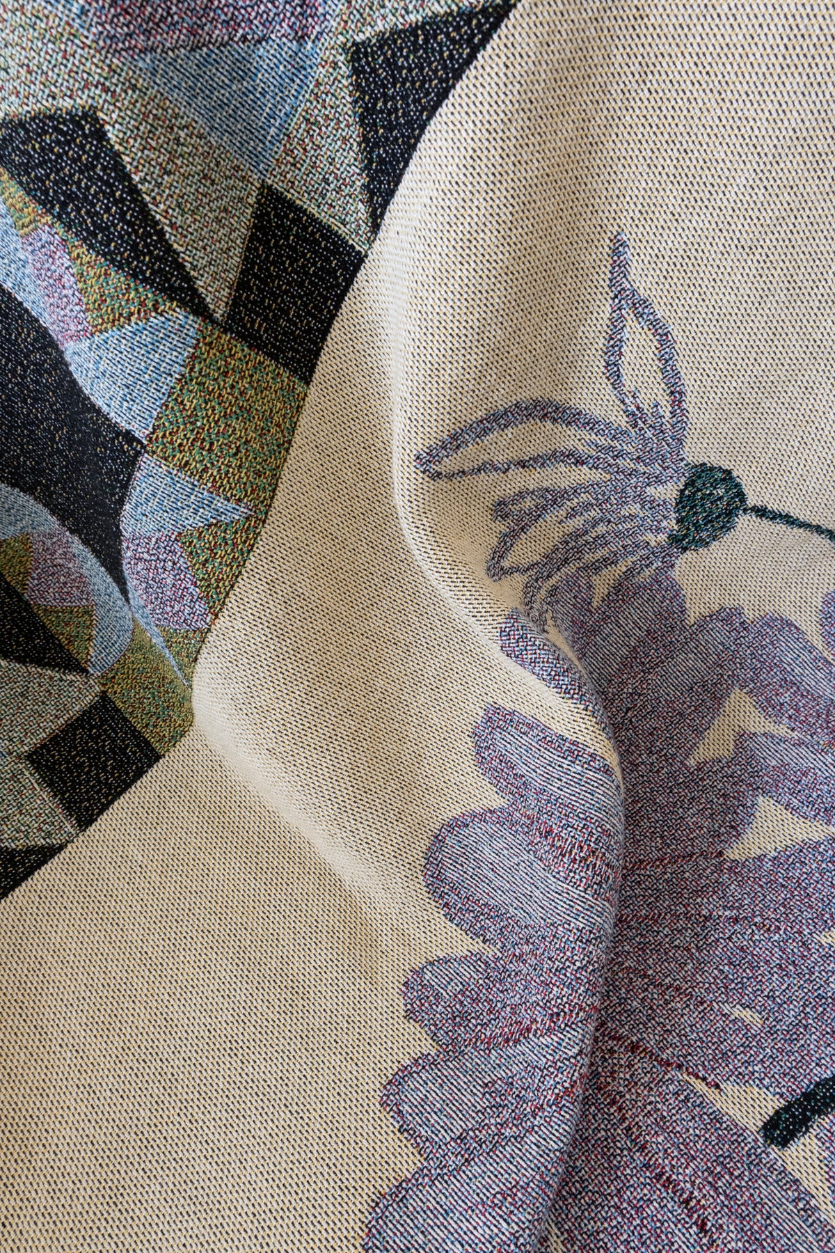 Close-up of a folded woven fabric blanket featuring a purple floral pattern and a geometric triangle design.