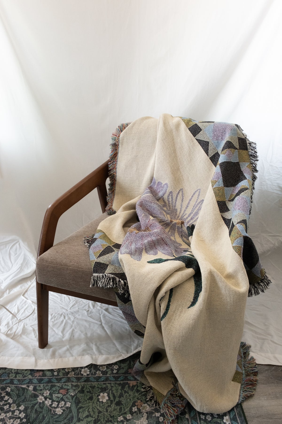 Cream woven fabric blanket with purple floral and geometric patterns draped over a wooden armchair.