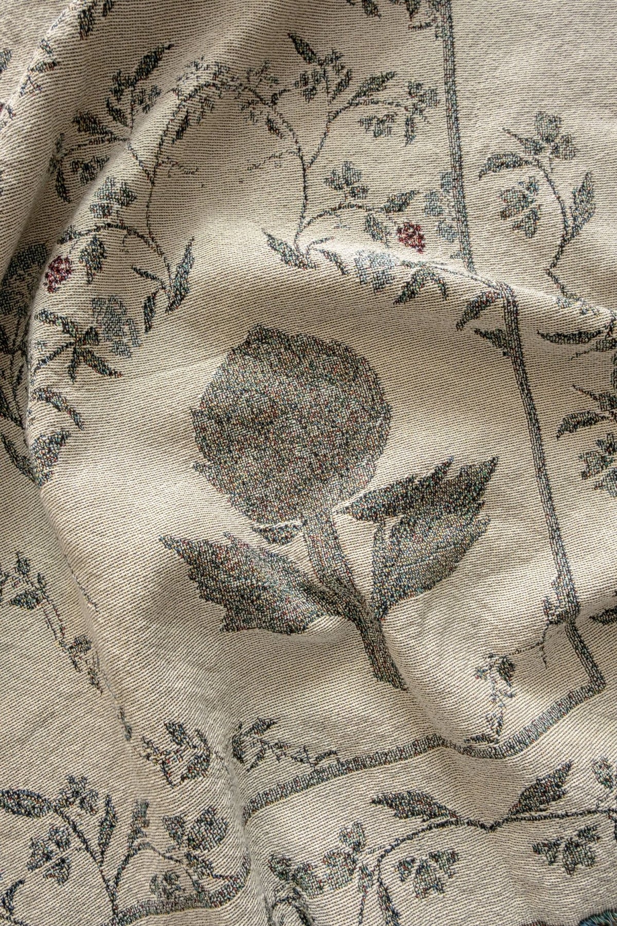 Artichoke woven blanket featuring a floral design with artichoke and vine motifs in muted colors on a light background.