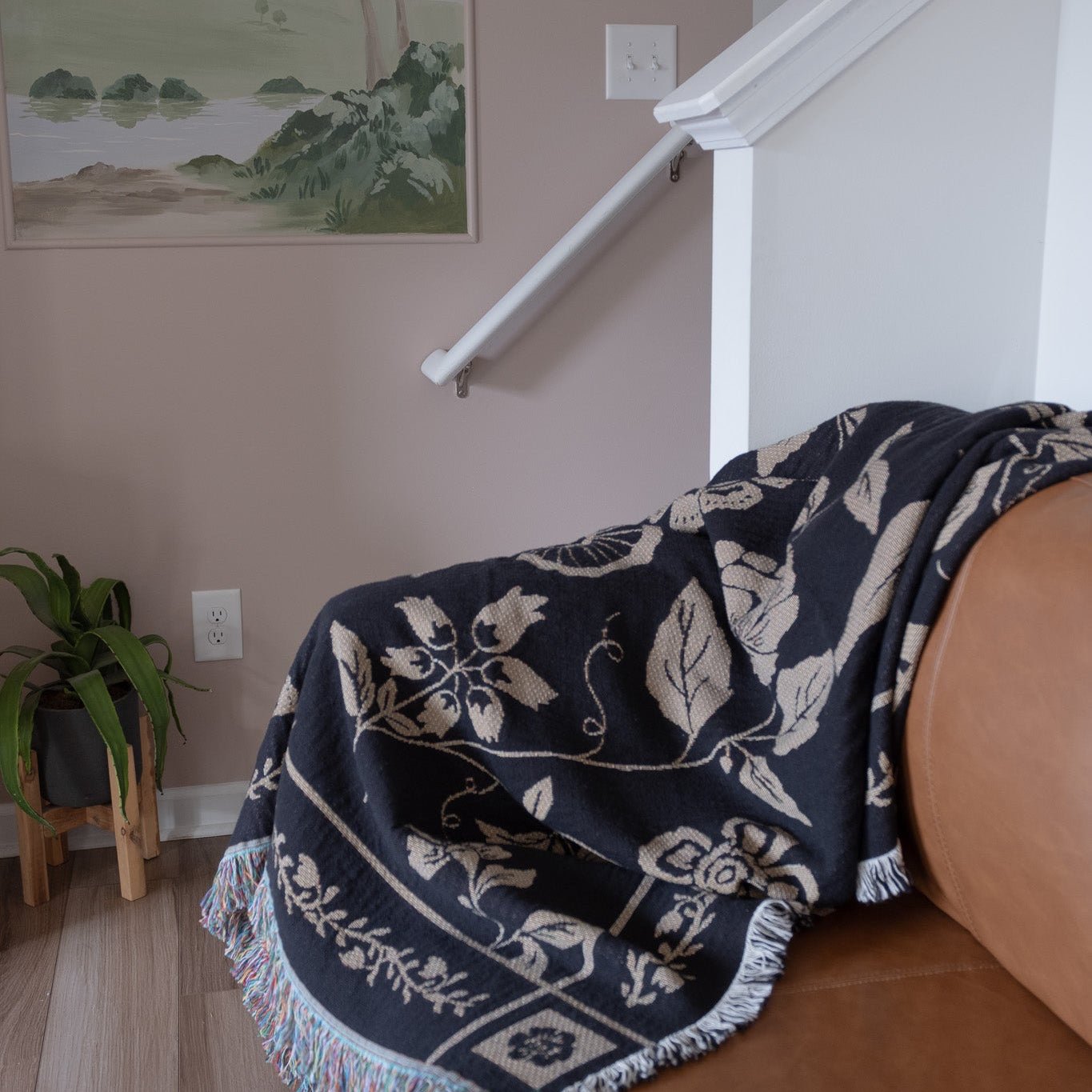 Bramble woven blanket in dark blue with floral patterns, draped over a brown leather sofa in a cozy living space.
