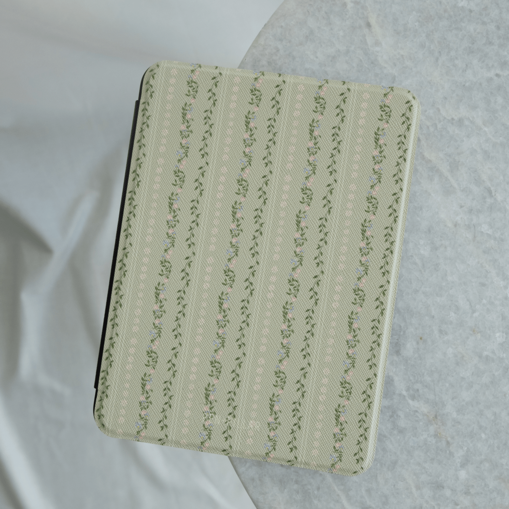 Camellia Kindle case with a light green floral pattern on a textured background, viewed from above.