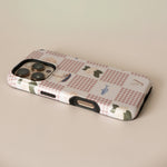 Coastal personalized iPhone case featuring a checkered pattern with boats and greenery, viewed from an angle.