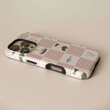 Coastal personalized iPhone case featuring a checkered pattern with boats and greenery, viewed from an angle.