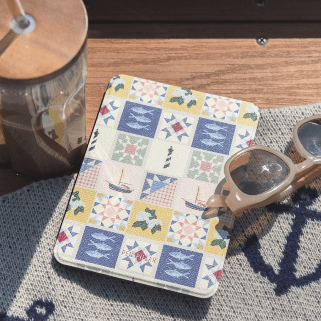 Rectangular Kindle case with a coastal quilt pattern featuring sailboats and fish, labeled PEN + PILLAR.