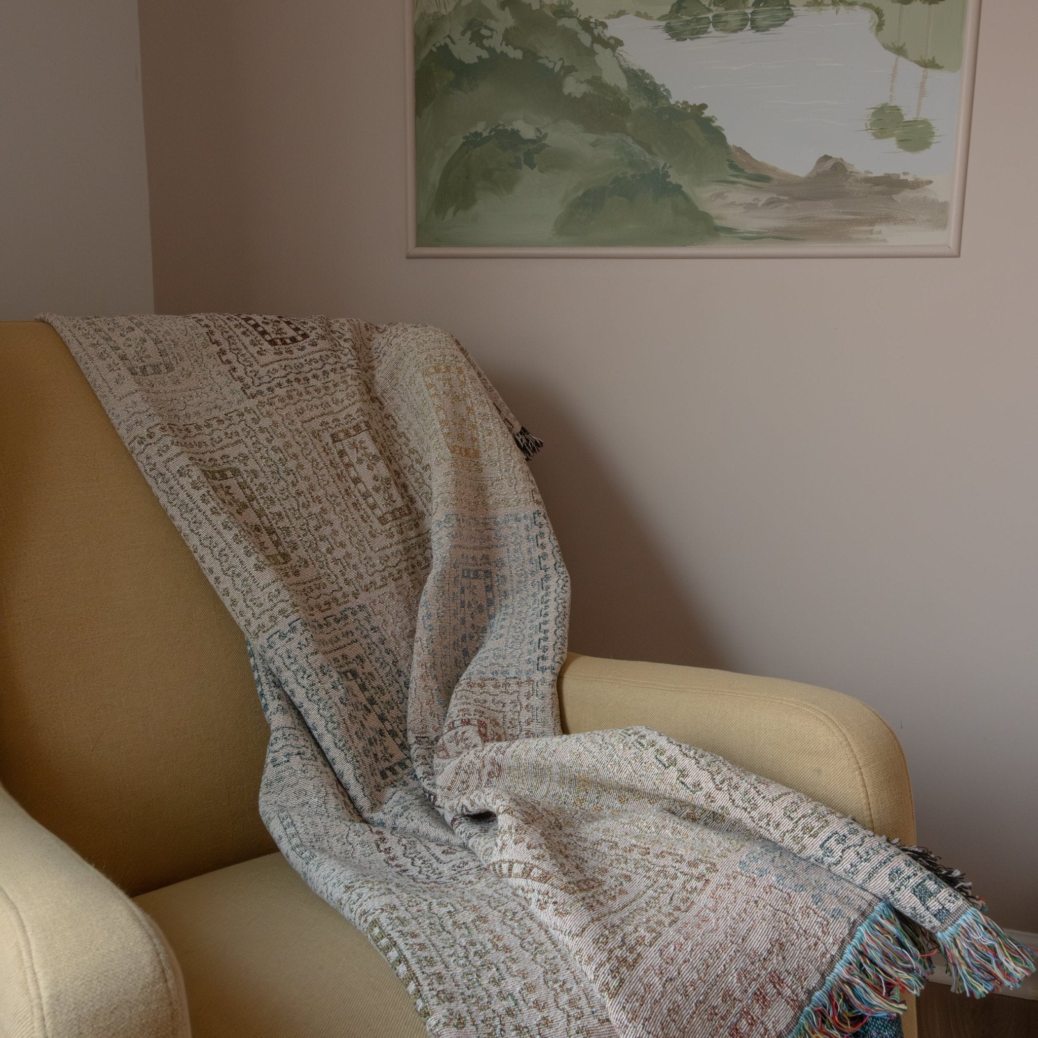 Curio woven blanket draped over a beige armchair, featuring intricate patterns and soft pastel colors.