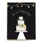 Decorative wedding card featuring a three-tier cake with floral accents and string lights, with the text "to the happy cou...
