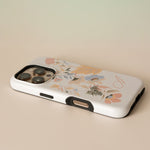 Fleur personalized iPhone case with floral design in pastel colors, angled view showing camera cutout and buttons.