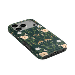 Forest iPhone case featuring floral and deer patterns on a dark green background, angled view showing buttons and ports.