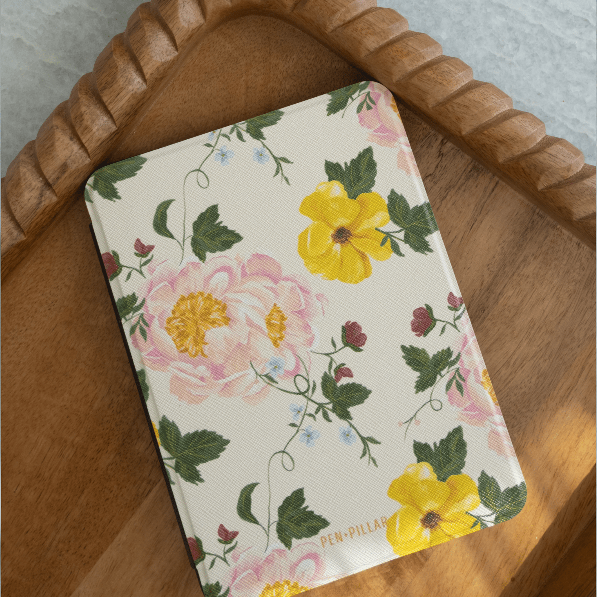 Garden Rose Kindle case featuring pink and yellow floral patterns on a cream background, placed on a wooden tray.
