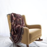 Garden rose woven blanket draped over a yellow rocking chair, featuring floral patterns in burgundy and green.