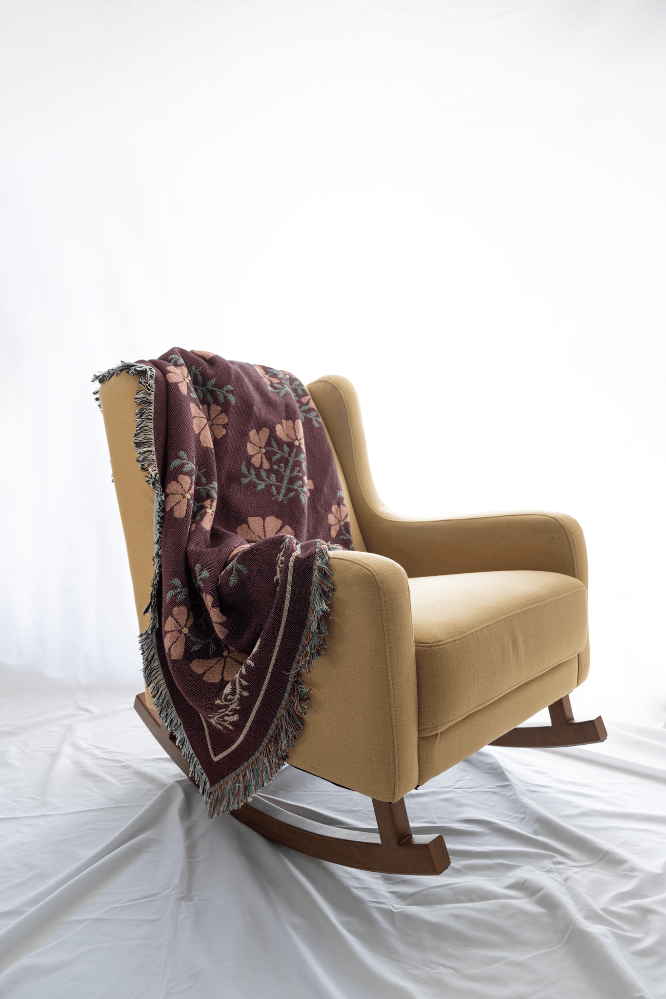 Garden rose woven blanket draped over a yellow rocking chair, featuring floral patterns in burgundy and green.