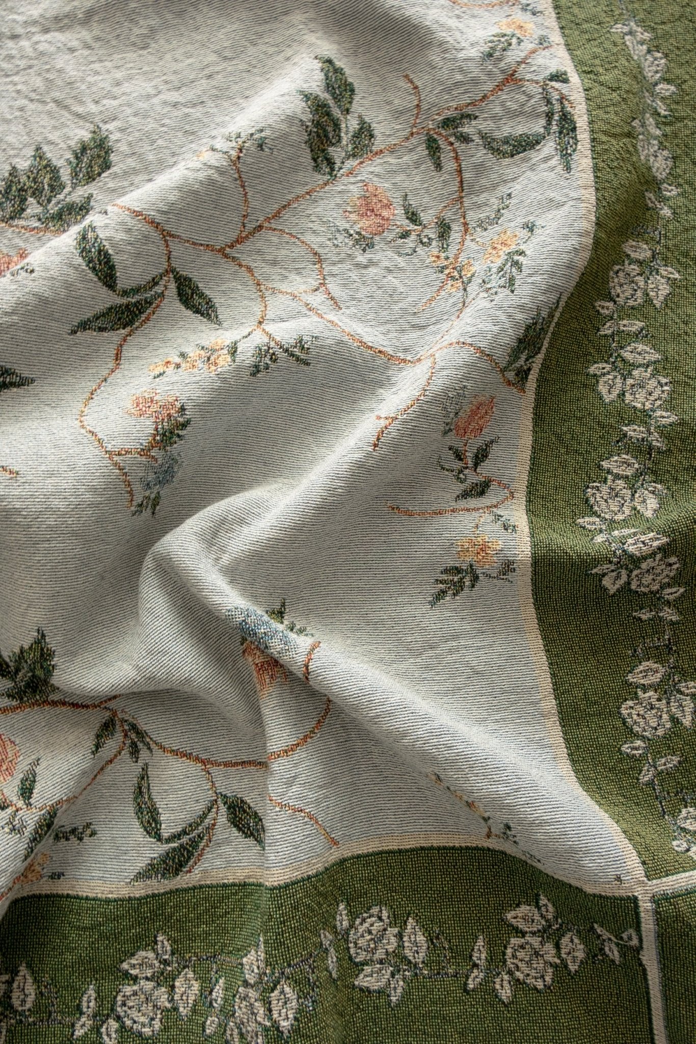 Grove woven blanket featuring floral patterns in soft colors on a textured fabric with green and cream tones.