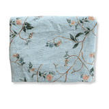 Grove woven blanket in light blue with floral patterns in pink and green, neatly folded.