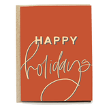 Happy Holidays card with orange background and gold cursive text on a textured kraft paper.