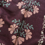 Haven woven blanket featuring a floral pattern in pink and green on a dark maroon background.
