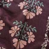 Haven woven blanket featuring a floral pattern in pink and green on a dark maroon background.