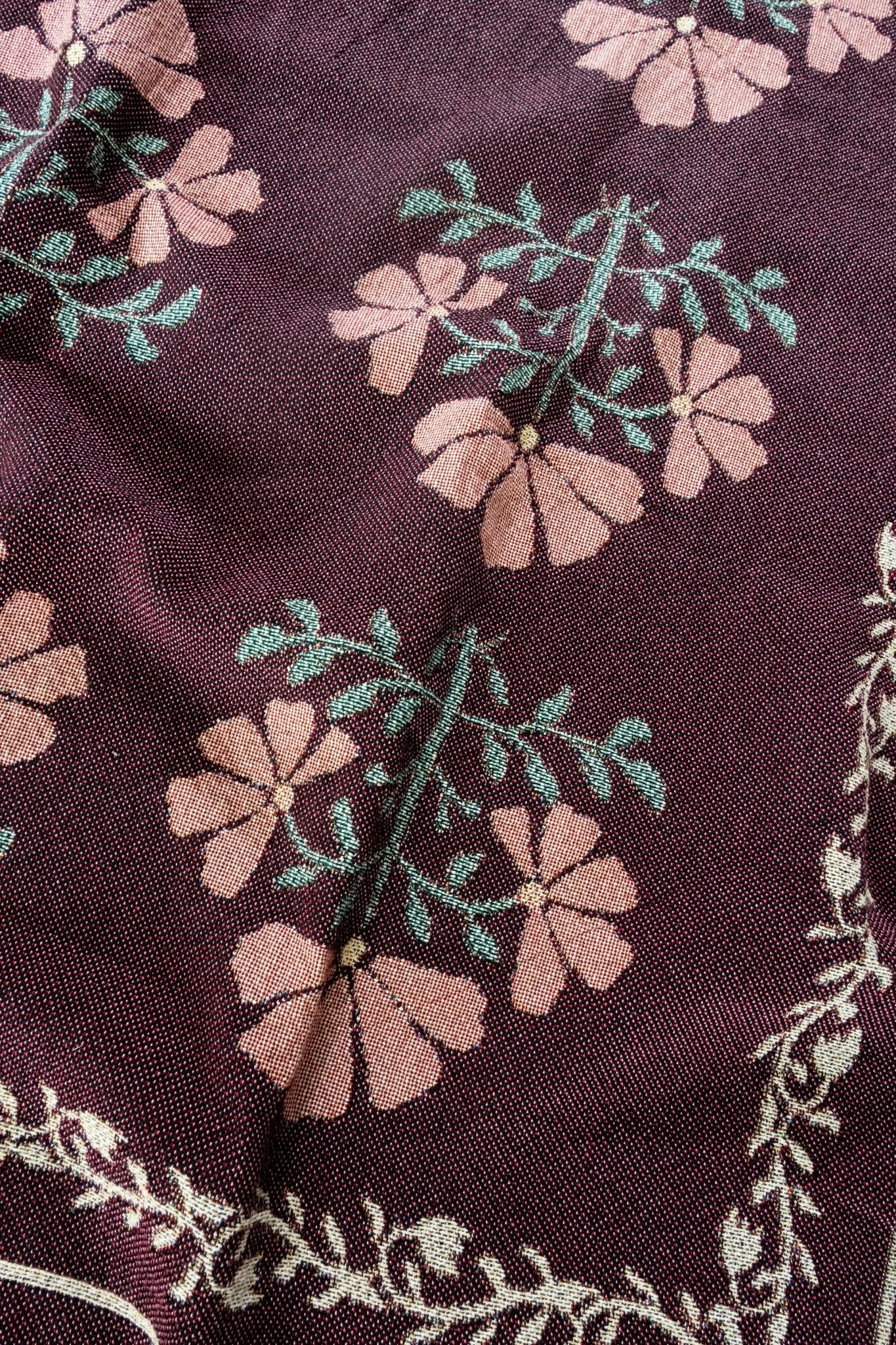 Haven woven blanket featuring a floral pattern in pink and green on a dark maroon background.