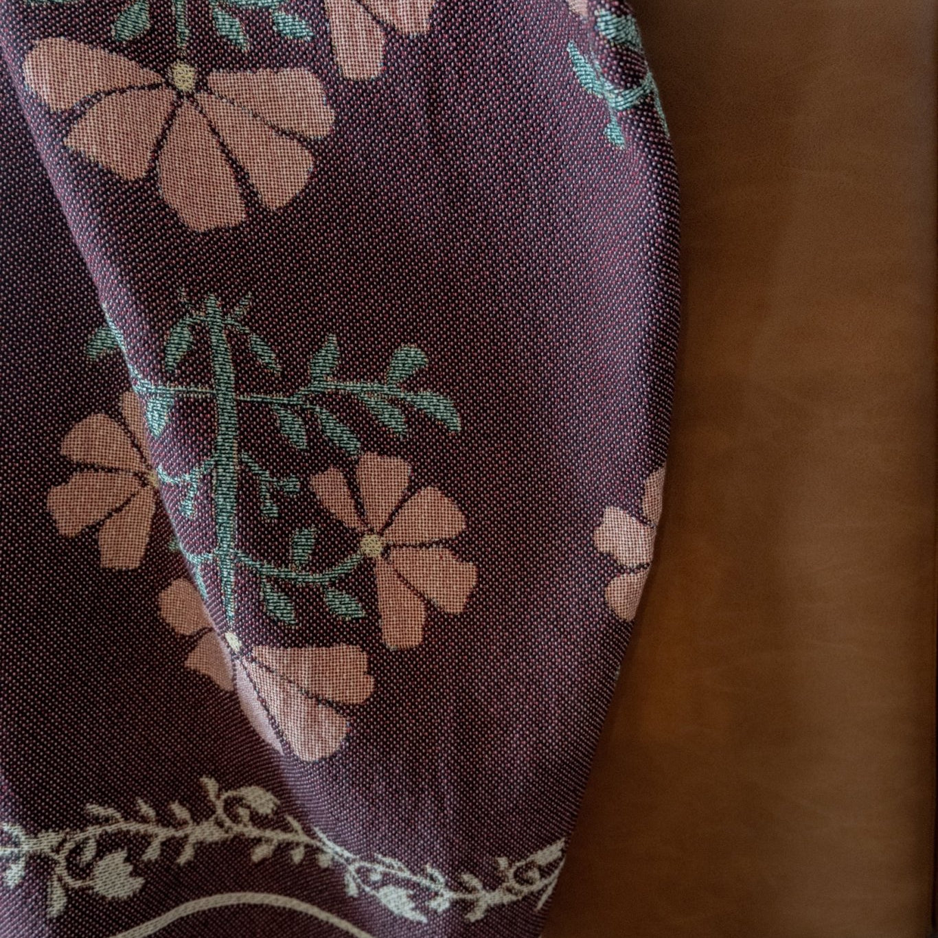 Haven woven blanket featuring floral patterns in pink and green, draped over a brown leather sofa.
