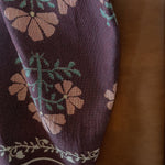 Haven woven blanket featuring floral patterns in pink and green, draped over a brown leather sofa.