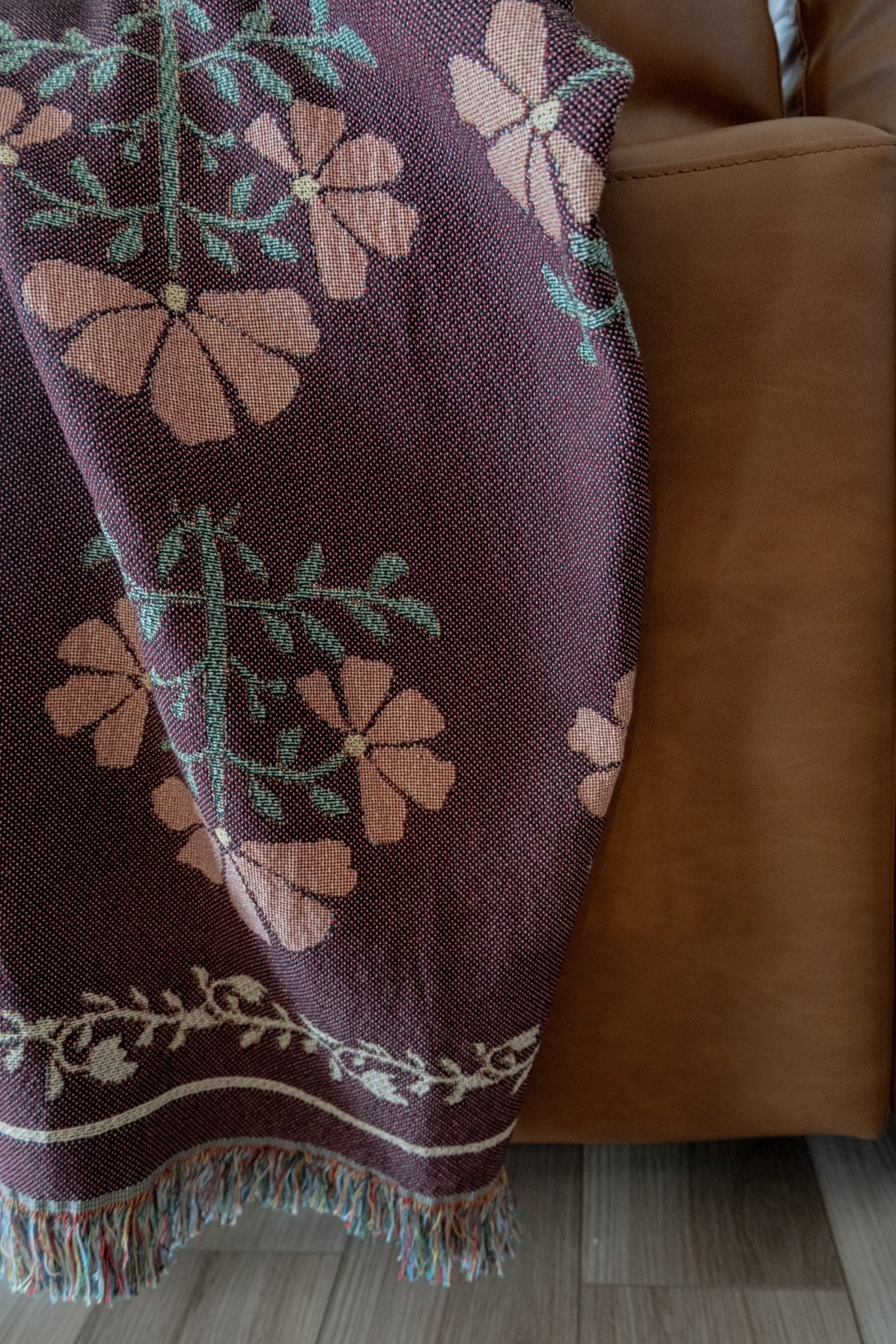 Haven woven blanket featuring floral patterns in pink and green, draped over a brown leather sofa.