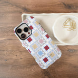 Heirloom iPhone case featuring a geometric pattern in red, blue, yellow, and white on a wooden surface.