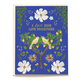 Love Birds Anniversary Card featuring two birds on a tree, surrounded by flowers and greenery on a blue background.